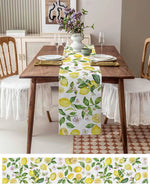 Une table élégante avec un chemin de table aux motifs de citrons et de feuilles vertes, entourée de chaises en bois et d'un vase de fleurs violettes, créant une ambiance chaleureuse et fraîche.