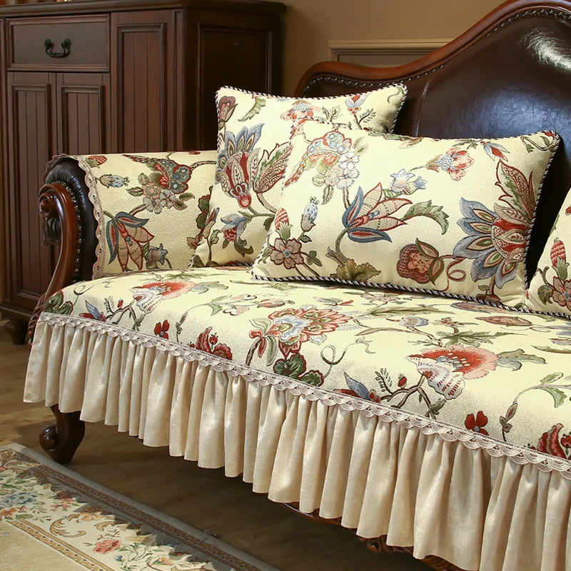 Un canapé en bois massif richement orné de motifs floraux colorés, avec des coussins assortis et une jupe de protection en dentelle, offrant un style élégant et douillet dans un espace cosy.