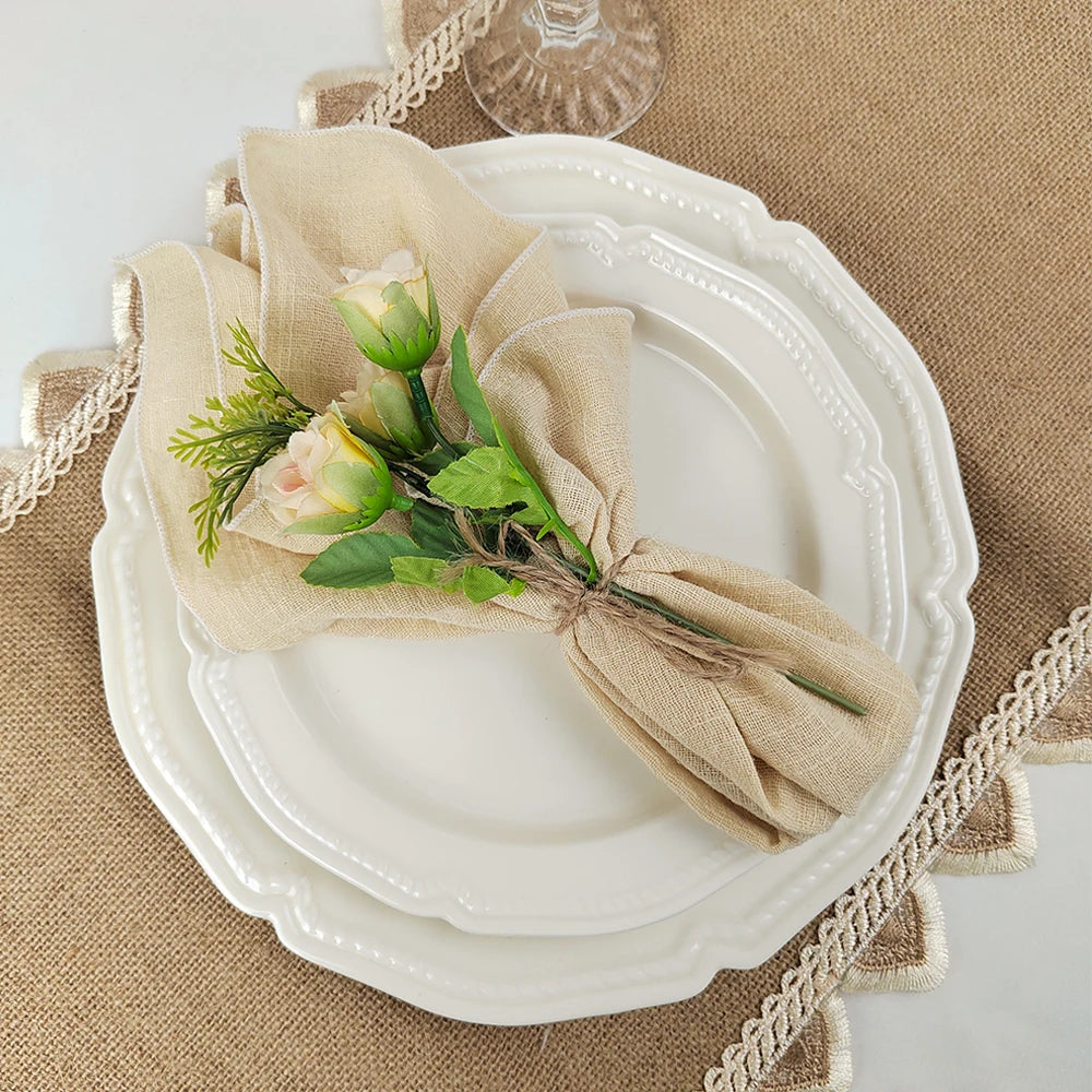 Une belle assiette blanche avec un bouquet de fleurs et de feuilles vertes enveloppé d'un linge de lin, posé sur un tapis de table beige.