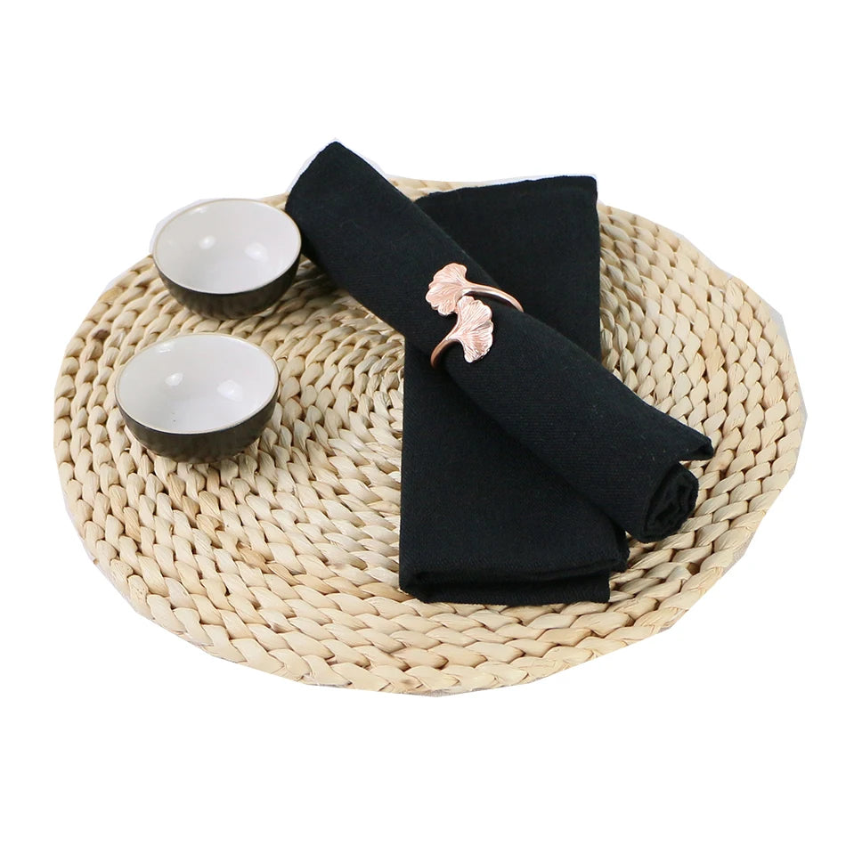 Des serviettes de table noires avec une décoration florale en métal rose sur un dessous de plat en fibres tressées.