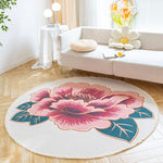 Un tapis rond décoratif avec un motif floral aux couleurs vives, posé dans un salon lumineux avec des meubles blancs et des touches végétales.