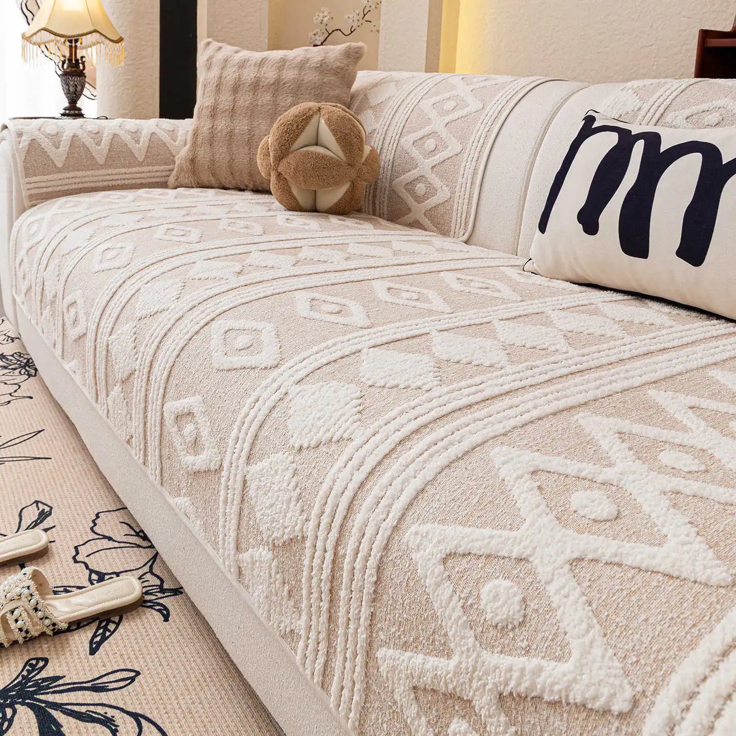 Cette image montre un canapé décoré avec un motif ethnique dans des tons beiges et blancs, avec des coussins et un oreiller décoratifs. Le canapé semble confortable et douillet dans cet environnement cocooning.