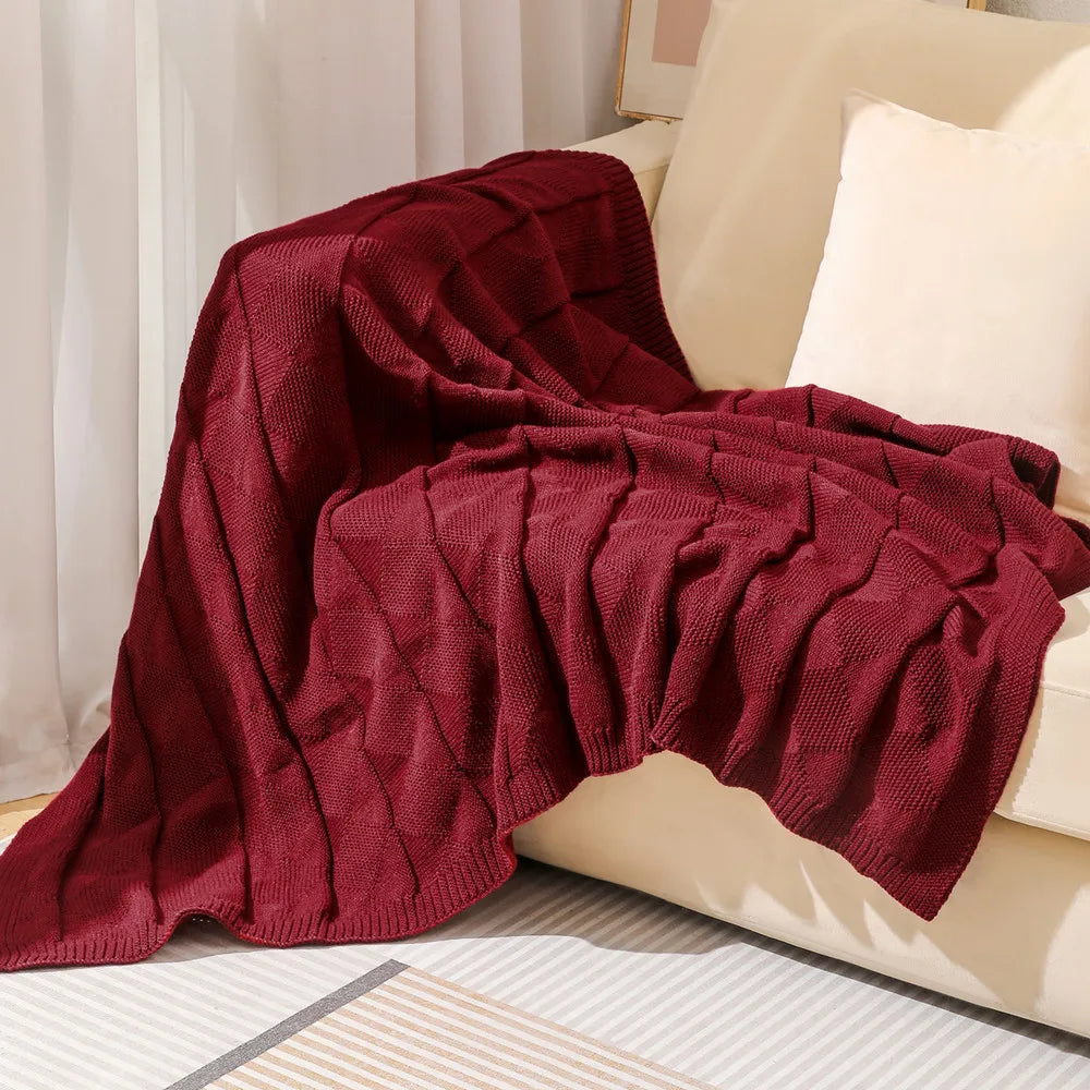 Couverture en tricot d'un riche rouge bordeaux, posée sur un canapé, créant une ambiance chaleureuse et accueillante.
