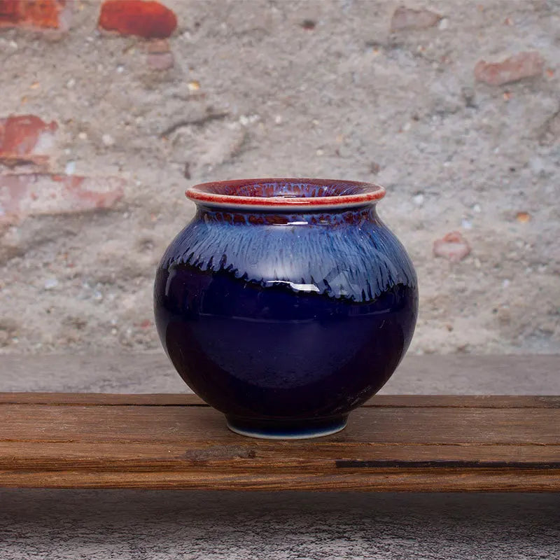 Un pot en céramique bleu foncé avec un rebord orange, posé sur une surface en bois, crée un contraste saisissant et met en valeur sa conception unique.
