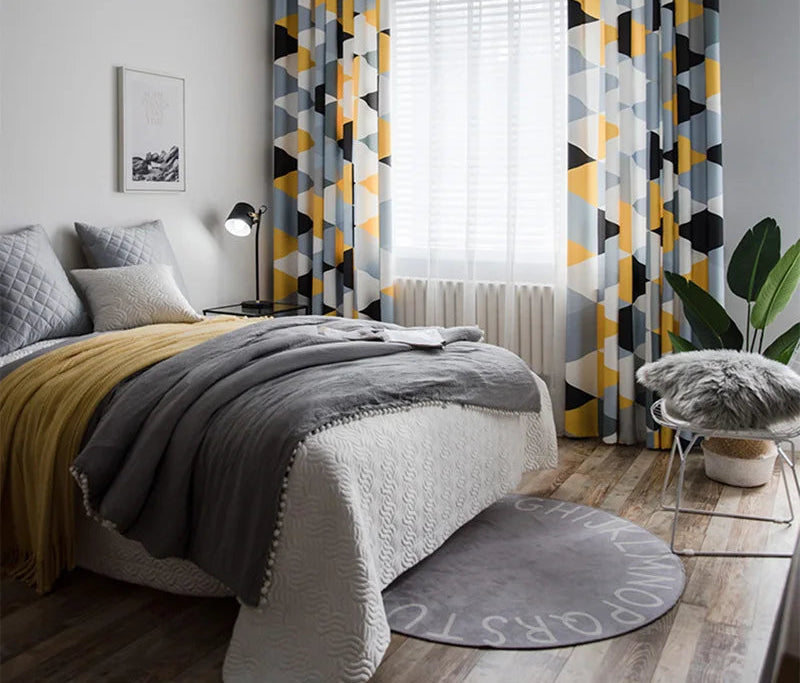 Chambre moderne au design scandinave avec rideaux géométriques colorés, lit confortable avec couverture grise et coussins assortis, tapis rond avec motifs alphabétiques, décoration lumineuse et plantes vertes pour une ambiance apaisante et contemporaine.