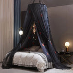 Un lit douillet avec un élégant baldaquin noir décoré de lumières et d'étoiles, créant une ambiance chaleureuse et invitante.