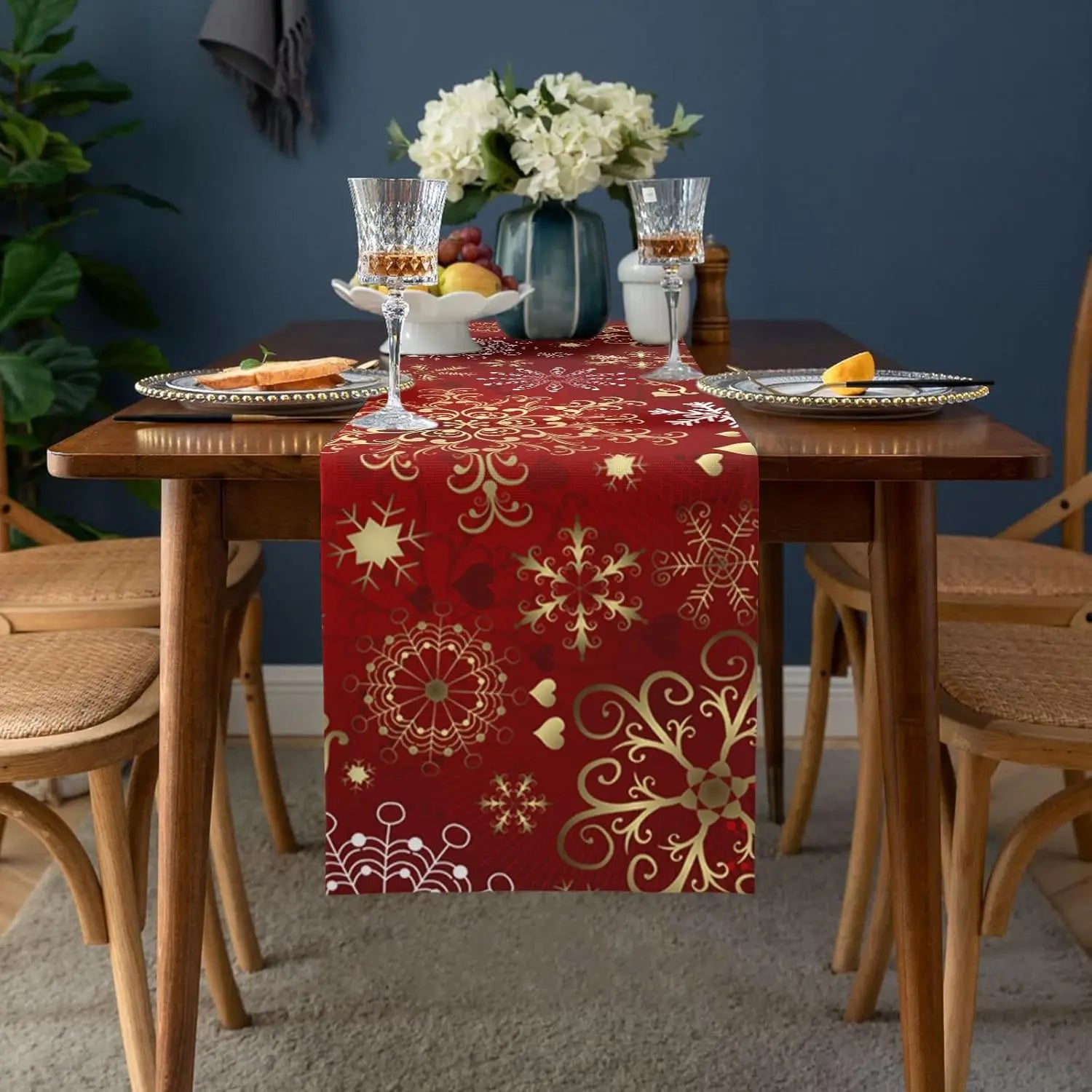 Une table joliment décorée avec une nappe rouge festive, un bouquet de fleurs, des verres et des fruits, créant une ambiance chaleureuse et conviviale.