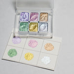 peintures aquarelle palette compacte bleu vert violet rose beige jaune blanc texture granuleuse opaques