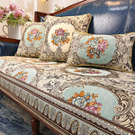 Cet image montre un beau canapé en cuir bleu foncé avec des coussins et une couverture décorés de motifs floraux élégants dans des tons pastel.