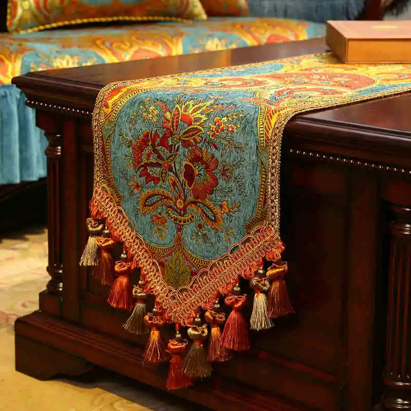 Cette image présente un magnifique chemin de table orné de motifs floraux colorés et de franges dorées, créant une atmosphère luxueuse et élégante.