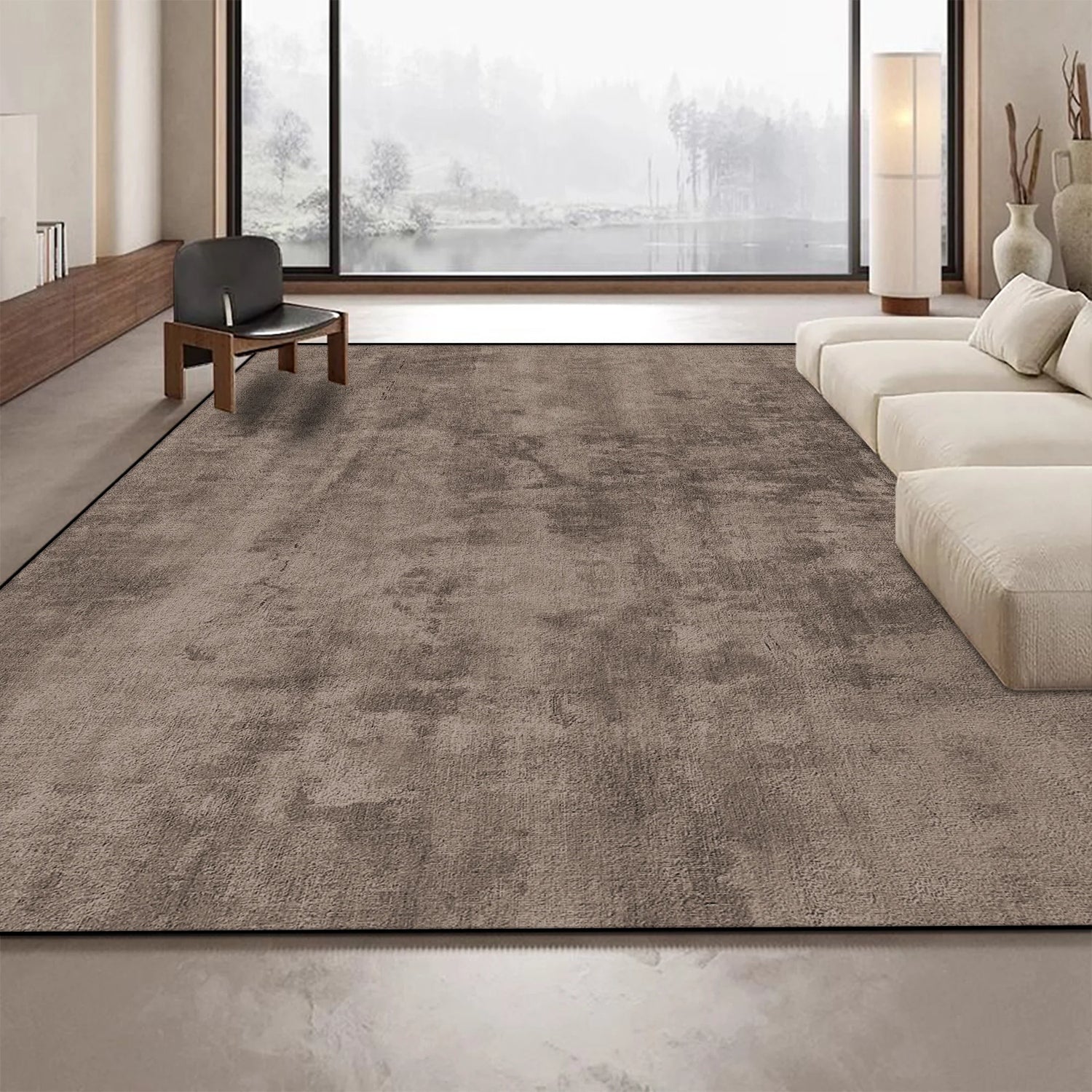 Cette image montre un beau tapis gris foncé placé sur un sol dans un salon lumineux avec une grande fenêtre offrant une vue sur un paysage extérieur.