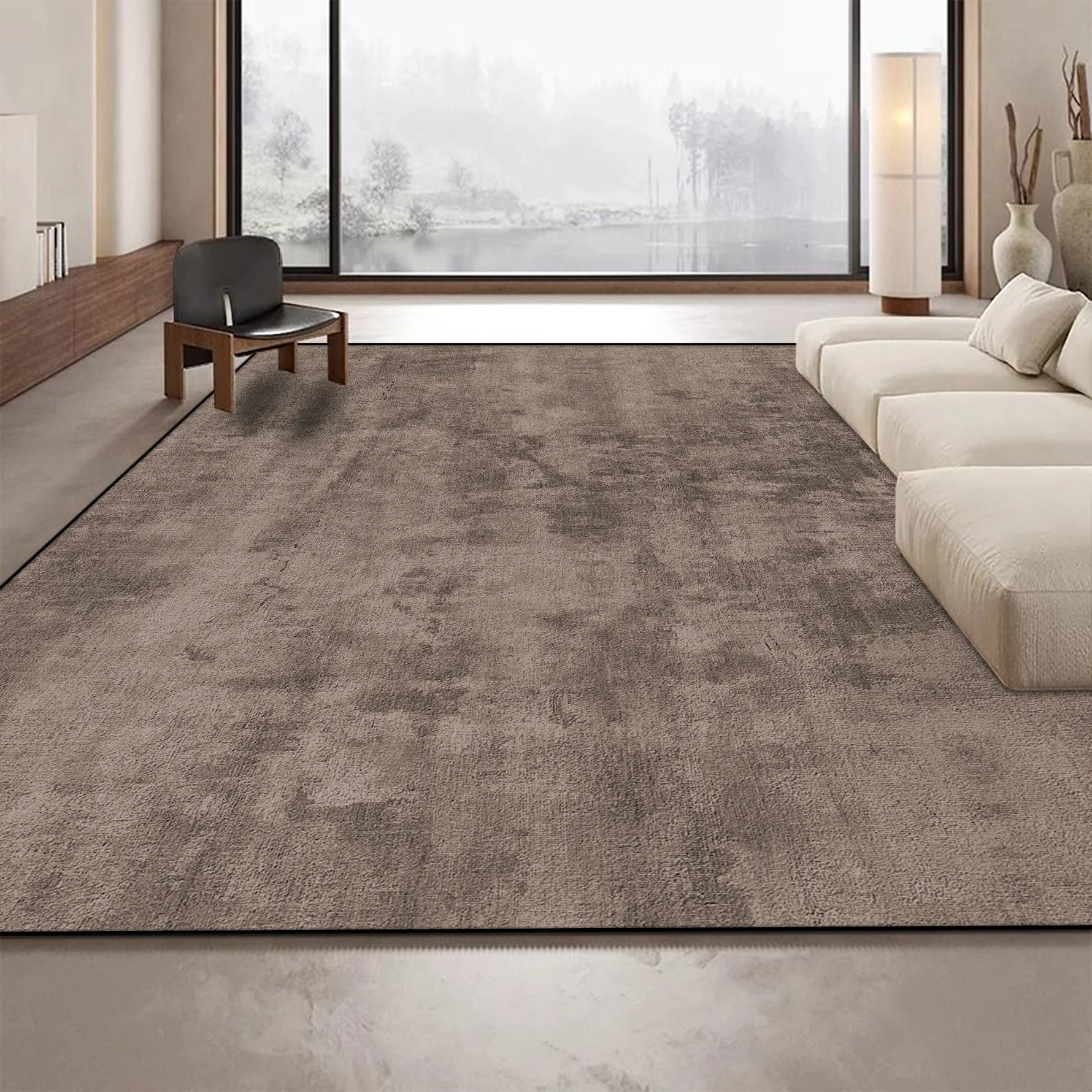Cette image montre un beau tapis gris foncé placé sur un sol dans un salon lumineux avec une grande fenêtre offrant une vue sur un paysage extérieur.