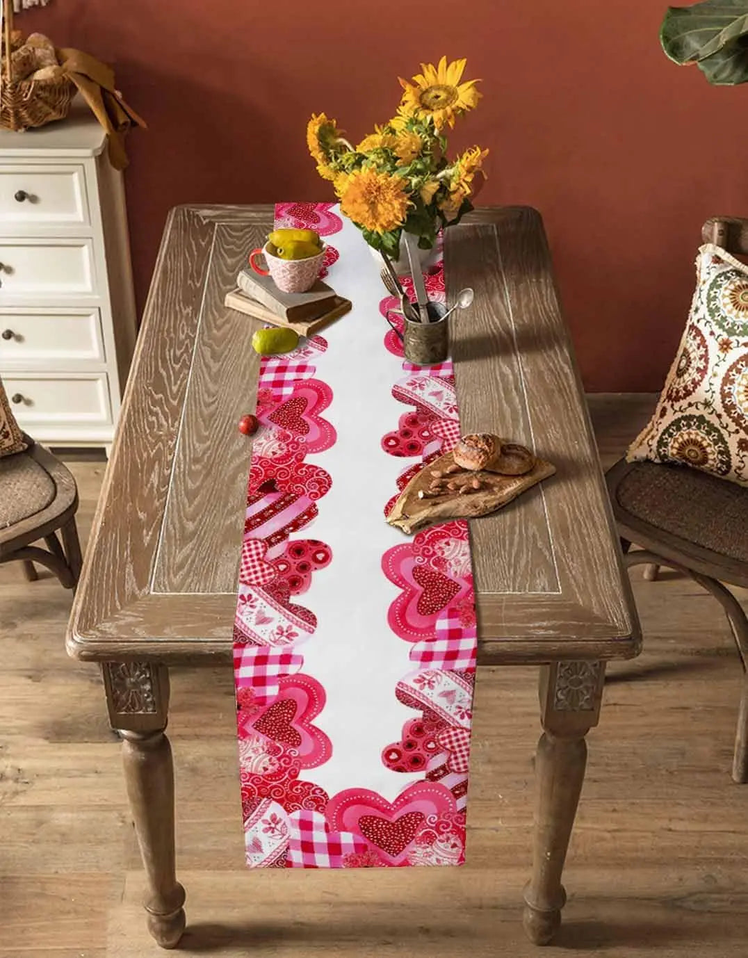 Une table en bois rustique avec un chemin de table rose orné de motifs en forme de coeur, un vase rempli de fleurs jaunes et des accessoires vintage.