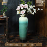 Un vase en céramique turquoise débordant de magnifiques fleurs blanches épanouis sur un fond sombre et boisé.