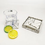 Un verre de cocktail rempli d'eau transparente sur un dessous de verre en marbre noir et blanc, accompagné de tranches de citron vert et de citron.