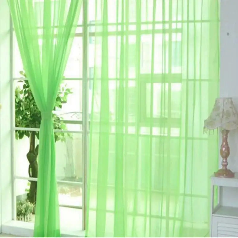 Voilage transparent vert pomme accroché à une grande baie vitrée, laissant passer la lumière naturelle dans un intérieur lumineux.