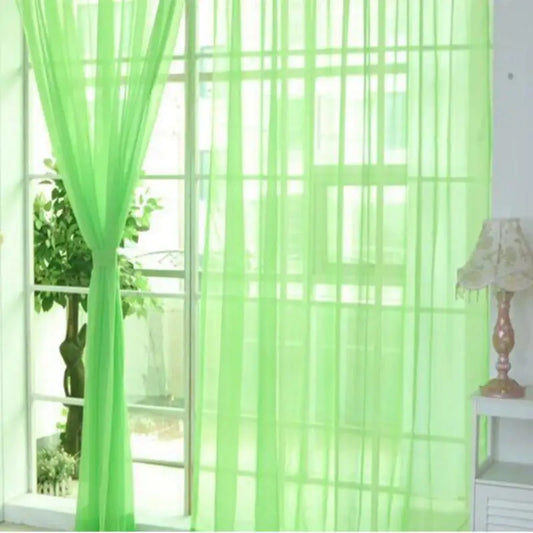 Voilage transparent vert pomme accroché à une grande baie vitrée, laissant passer la lumière naturelle dans un intérieur lumineux.