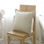 Un coussin blanc repose confortablement sur une chaise en bois dans un intérieur lumineux et épuré.