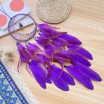 Un attrape-rêves magnifique violet et pourpre, avec des plumes délicates et des perles noires, posé sur une surface en bois avec des motifs ethniques.