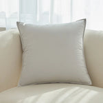 Un oreiller en gris clair placé sur un canapé beige, dans un environnement lumineux.