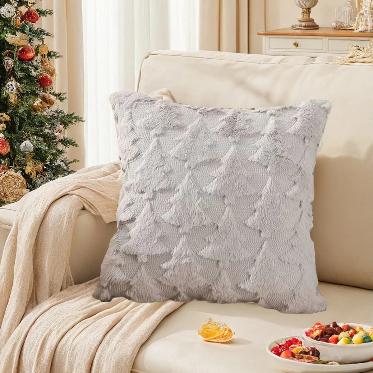 Coussin moelleux gris orné de motifs texturés, sur un canapé beige dans un salon décoré pour Noël avec un arbre de Noël et des décorations festives.