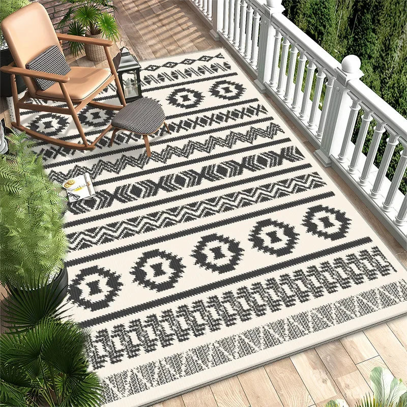 Tapis extérieur en noir et blanc avec un motif géométrique ethnique sur un balcon en bois avec des plantes vertes.