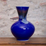 Vase en céramique bleu foncé avec des motifs abstraits et une forme arrondie, posé sur une surface en bois.