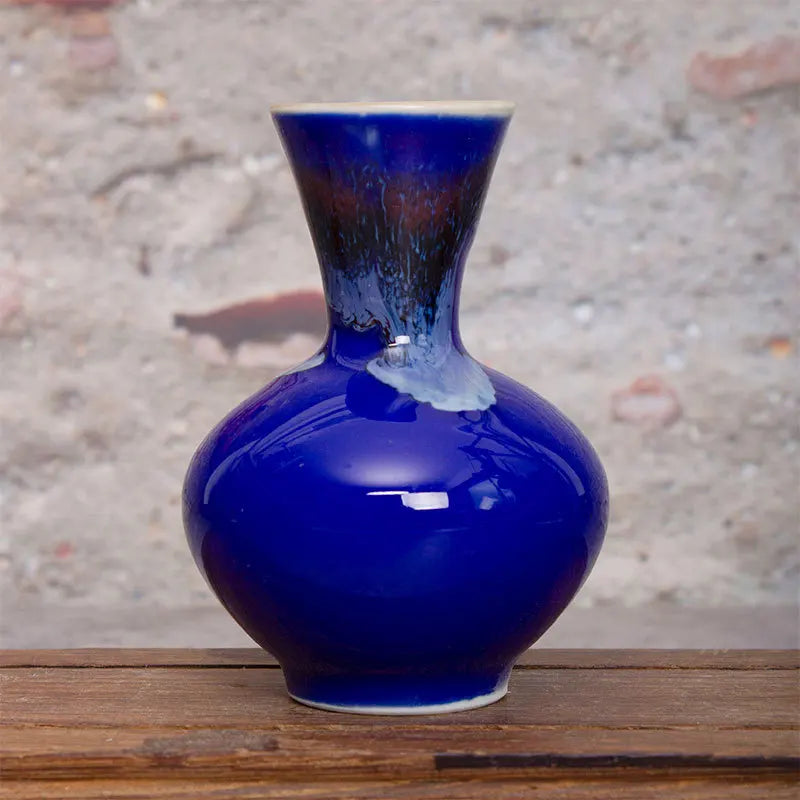Vase en céramique bleu foncé avec des motifs abstraits et une forme arrondie, posé sur une surface en bois.