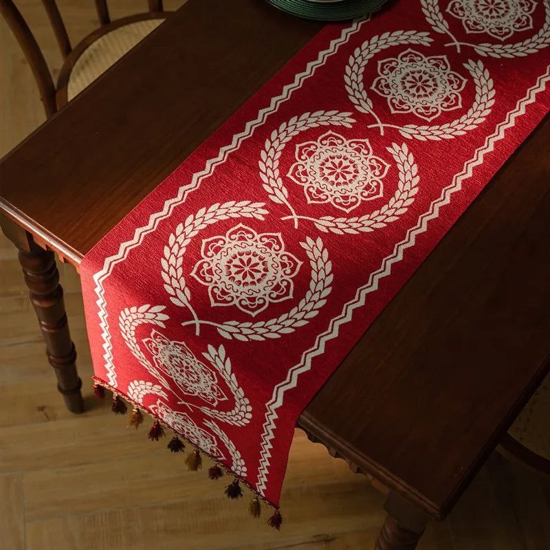 Une nappe en tissu rouge ornée de motifs floraux blancs élégants, offrant une touche traditionnelle et chaleureuse à cette table en bois.