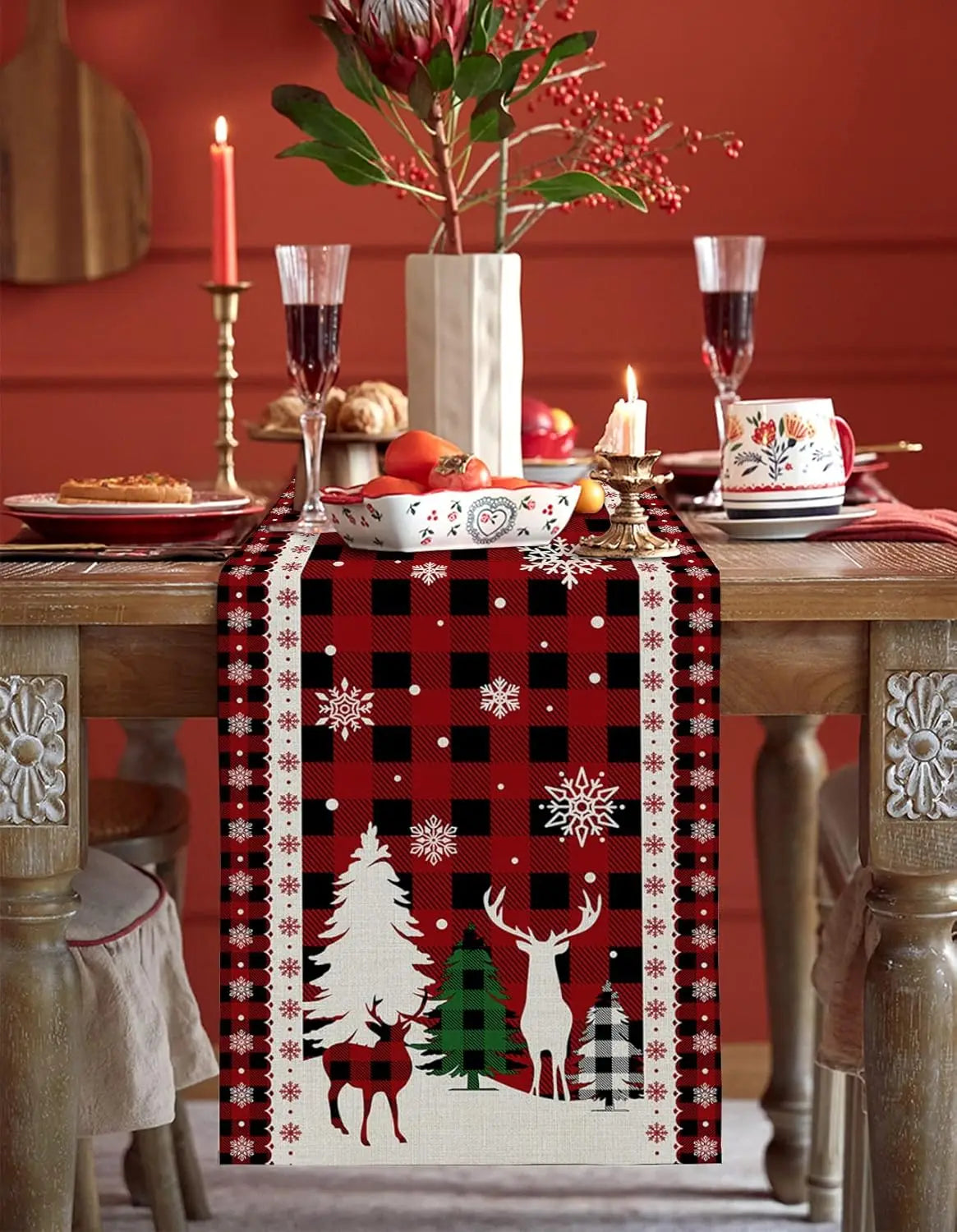 Une table de fête de Noël décorée avec un centre de table festif, des bougies, des verres de cristal et une nappe à motifs de cerfs et de sapins.