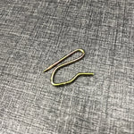 Un crochet à rideau en métal doré posé sur une surface grise texturée.