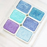 peintures aquarelle palette compacte bleu vert violet rose beige jaune blanc texture granuleuse opaques
