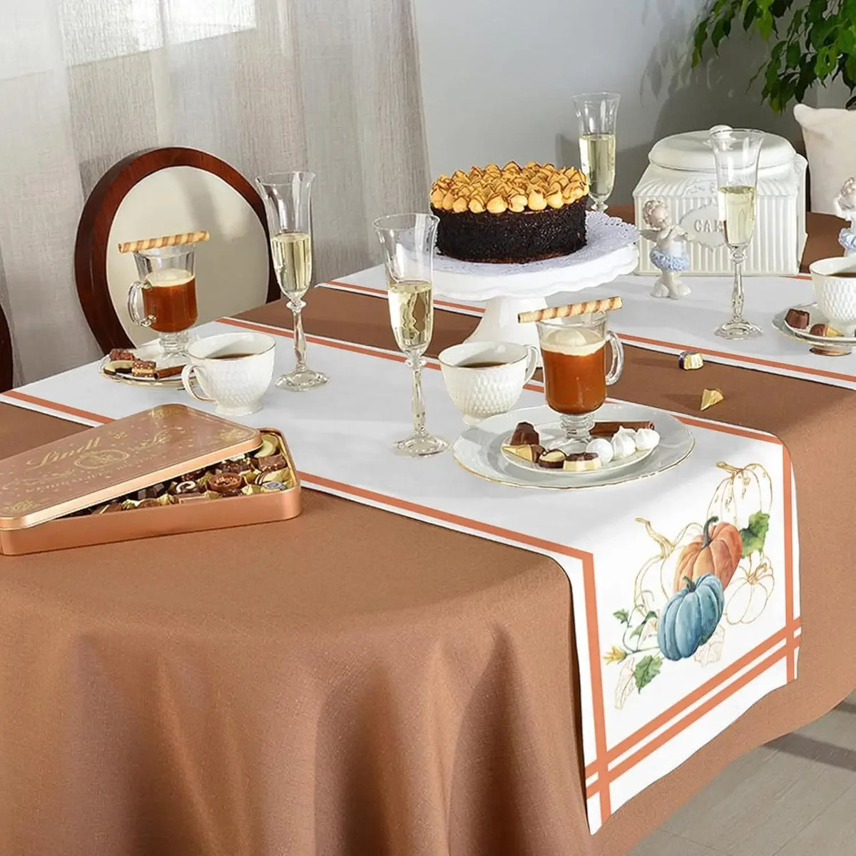 Une table élégante avec un gâteau chocolat garni de guimauves, des verres de champagne et des boîtes de bonbons dans une décoration automnale.