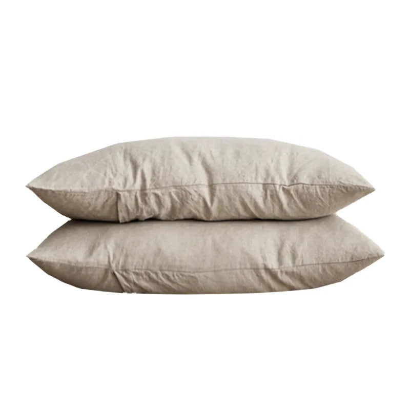 Deux oreillers en lin beige superposés sur fond blanc.