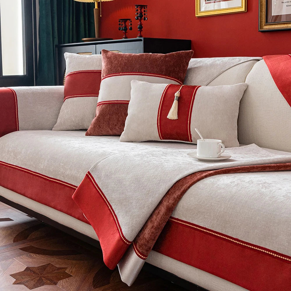 Un canapé confortable avec des coussins rouges et beiges, posé sur un sol en bois, dans une pièce aux murs rouges.