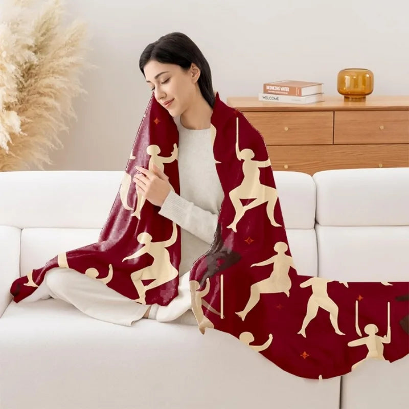 Femme assise confortablement sur un canapé, enveloppée dans une couverture rouge ornée de silhouettes blanches représentant des personnes.