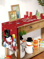 Cette image représente une scène de Noël avec des décorations, des bougies rouges, un chemin de table rouge orné de flocons de neige, et deux figurines de bonhommes de neige, le tout sur un meuble en bois.