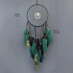 Un capteur de rêves orné de plumes de paon vertes et noires, de perles et de plumes décoratives, suspendu par un anneau en métal noir.