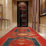 Couloir luxueux avec un magnifique tapis rouge orné de motifs floraux et ethniques, encadrant une porte en bois sombre à l'entrée.