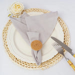 L'image montre une table de service élégante avec une assiette blanche, des couverts en métal, un napperon tressé et une serviette de table beige ornée d'un bouton en osier, ainsi qu'une belle rose jaune sur le côté.