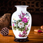 Vase en porcelaine blanche décoré de fleurs de pivoines et de motifs d'oiseaux, sur un support en bois foncé.