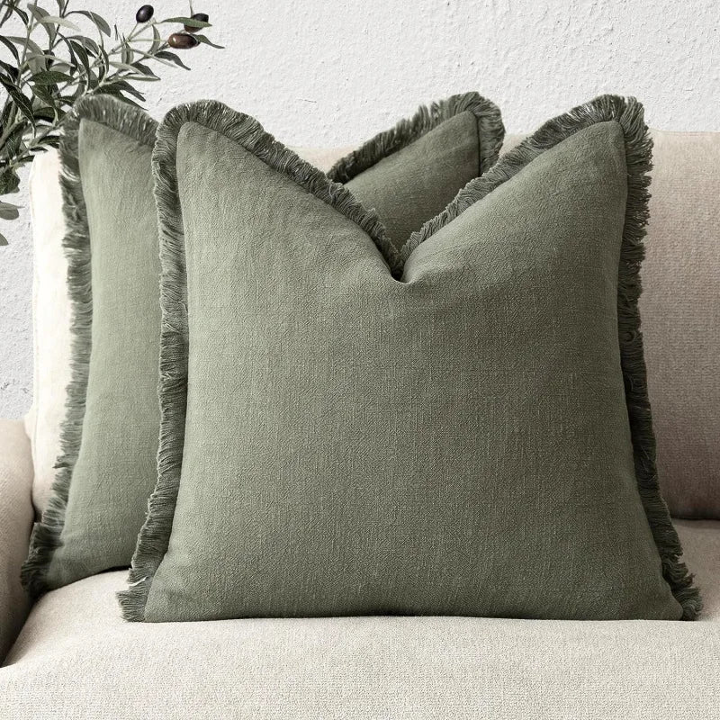 Coussin décoratif gris avec une bordure frangée posé sur un canapé dans un intérieur minimaliste.