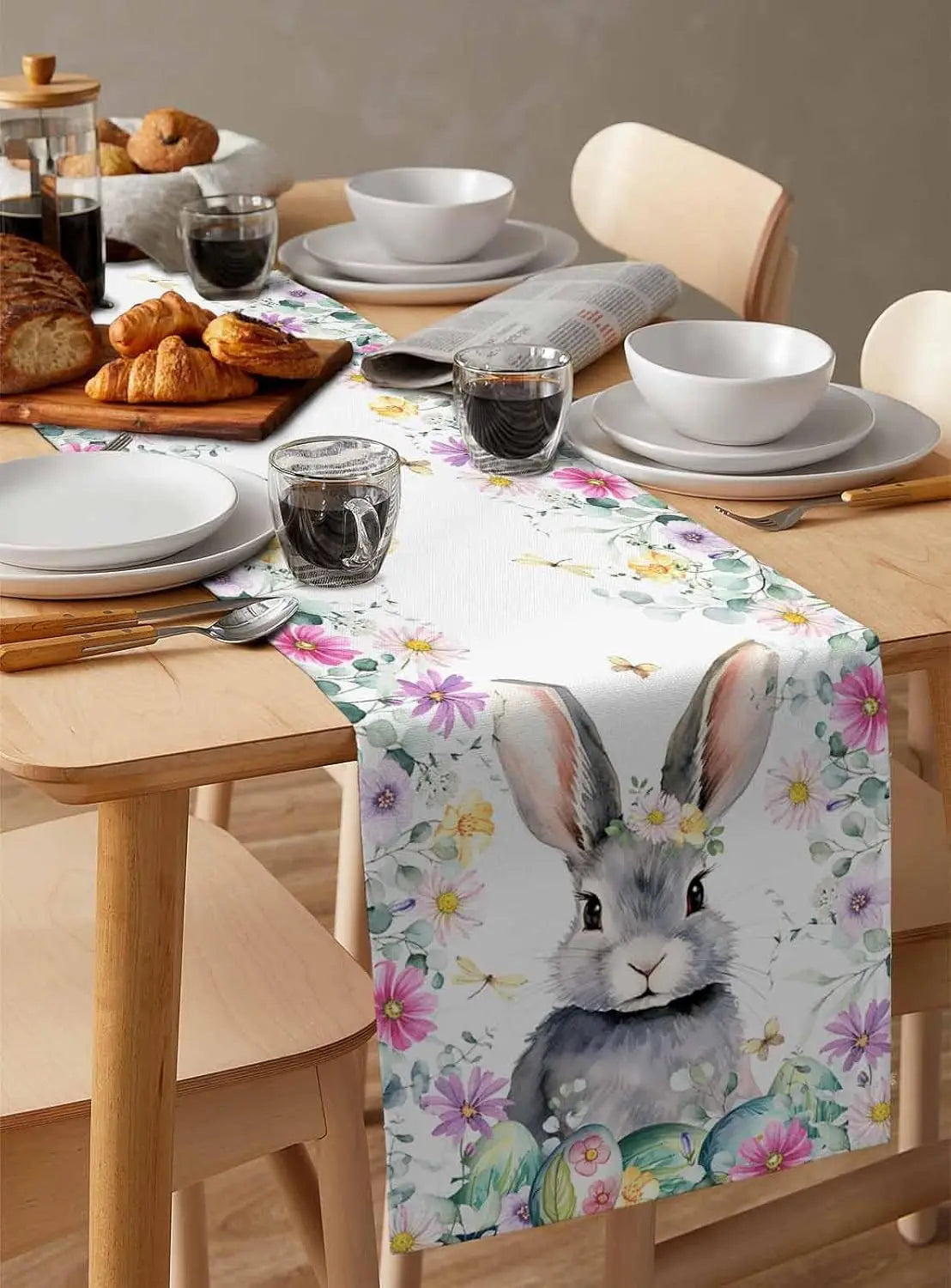 Une belle table de petit-déjeuner avec des croissants, des verres et une jolie nappe à motifs floraux avec un adorable lapin.