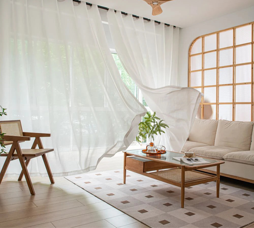 Voilage blanc opaque flottant dans un salon lumineux avec mobilier en bois clair et décoration naturelle.