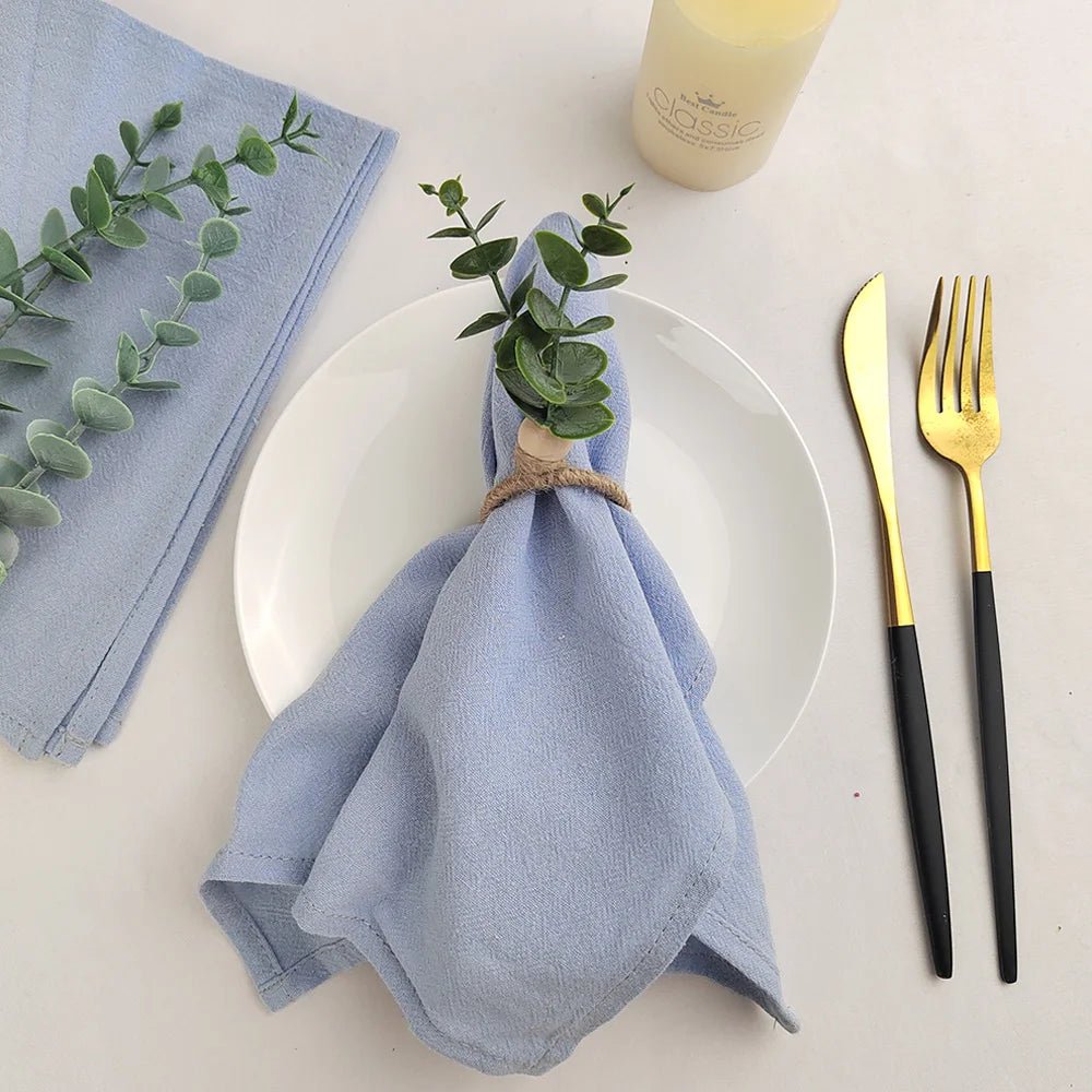 Un arrangement de serviette décorative avec des eucalyptus, une bougie et des couverts dorés sur une table blanche.