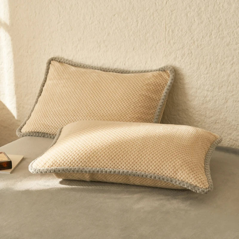 Deux oreillers beiges texturés avec bordure grise, posés sur un canapé blanc, créant une atmosphère apaisante et confortable.