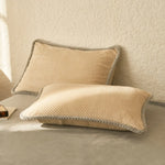 Deux oreillers beiges texturés avec bordure grise, posés sur un canapé blanc, créant une atmosphère apaisante et confortable.