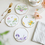 Assiettes en porcelaine de style vintage ornées de délicates fleurs peintes à la main, accompagnées d'ustensiles dorés et d'accessoires décoratifs.