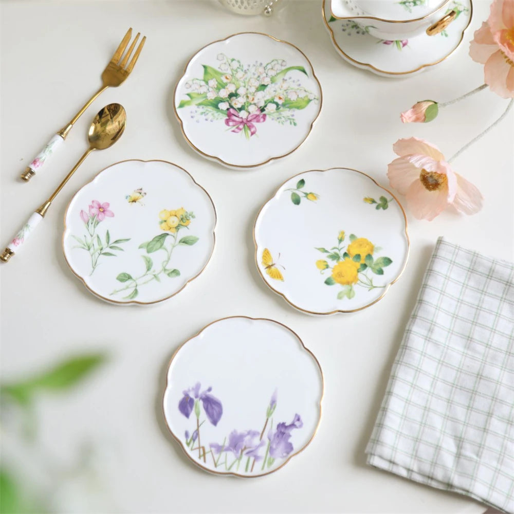 Assiettes en porcelaine de style vintage ornées de délicates fleurs peintes à la main, accompagnées d'ustensiles dorés et d'accessoires décoratifs.