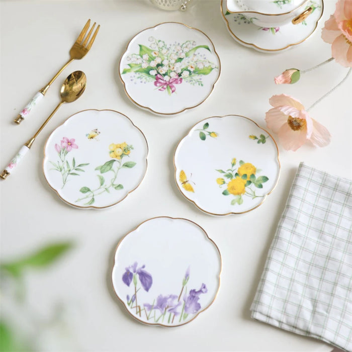 Assiettes en porcelaine de style vintage ornées de délicates fleurs peintes à la main, accompagnées d'ustensiles dorés et d'accessoires décoratifs.